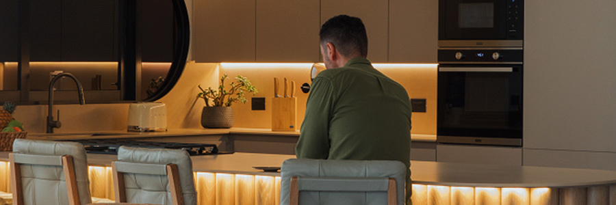 Modern Kitchen Scene with Warm Lighting Modern kitchen interior with under-cabinet and island lighting, man sitting at counter