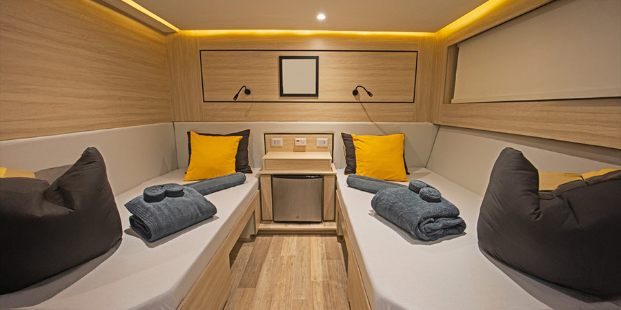 led-lighting-interior-boat-cabin-modern-design A modern boat cabin featuring LED strip lighting along the ceiling, warm wood finishes, twin beds with yellow pillows, and neatly folded towels for a cozy interior.