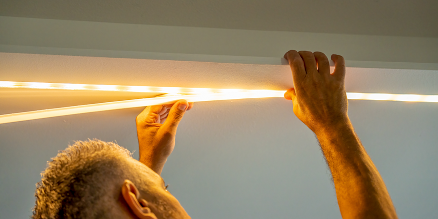 man-installing-led-strip-lights-on-ceiling Man installing LED strip lights on a ceiling, securing a diffuser cover to evenly distribute the warm light.