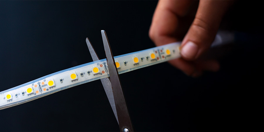 person-cutting-led-strip-with-scissors A close-up of a person using scissors to cut an LED strip at a marked cutting point, demonstrating easy customization for lighting projects.