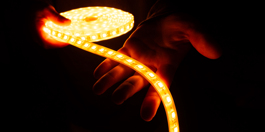 person-holding-illuminated-led-strip-in-dark Person holding a glowing LED strip light emitting warm orange light in a dark setting.