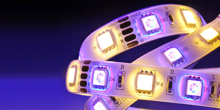 A close-up view of an RGBW LED strip showcasing its individual diodes emitting bright white and purple light on a dark background.