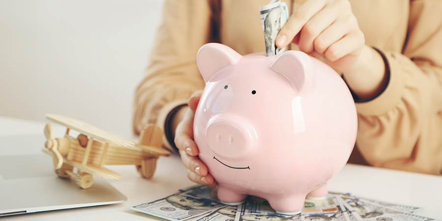 Pink piggy bank with cash and a wooden airplane on a white table