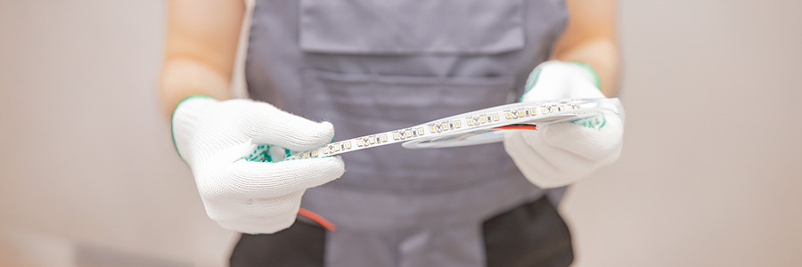 technician-handling-led-strip-light-roll-for-installation A close-up of a technician wearing gloves and holding a roll of LED strip light, showcasing the individual LED components and wiring.